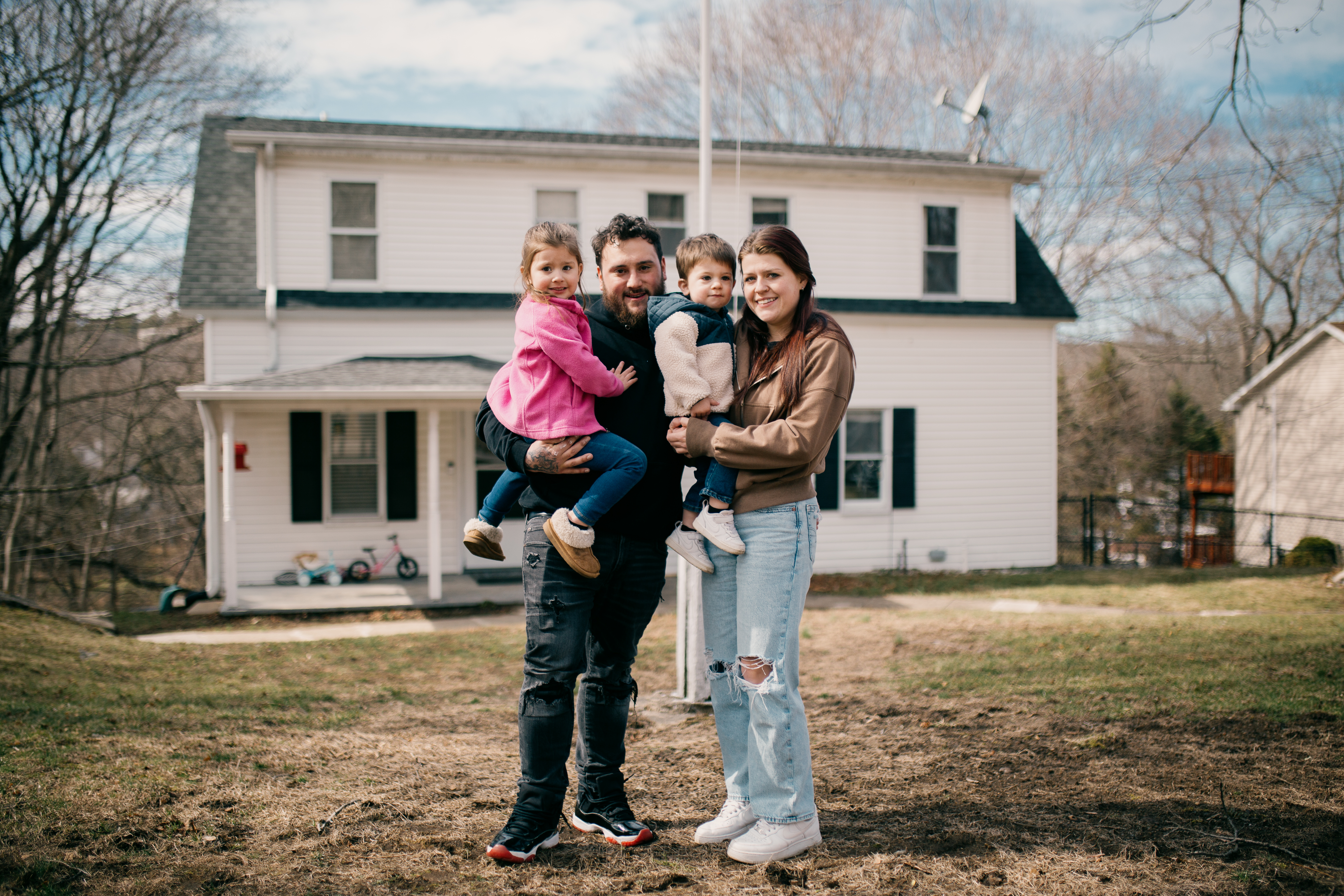 Self-Help borrower, Dominic, standing in front of his house with his wife and two kids