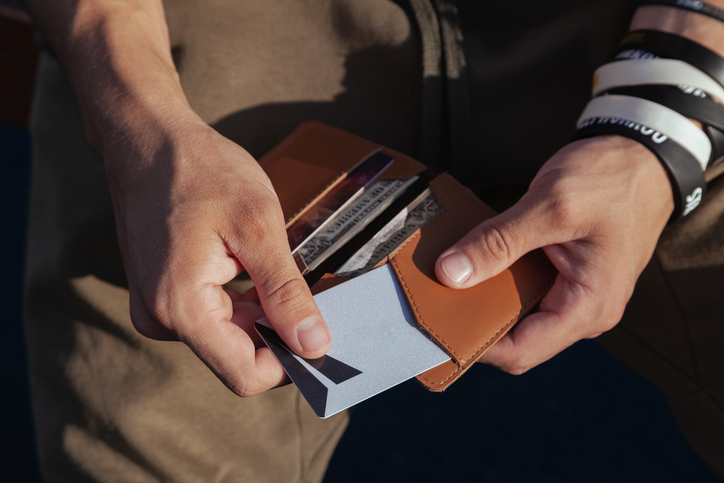 A person in sportswear is holding a small comfortable red leather wallet in his hands and takes out a plastic card, top view. Horizontal orientation, copy space, close-up, no face.